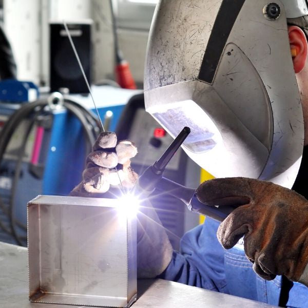 A man using TIG welding to weld a metal box. The man is wearing a welding mask.